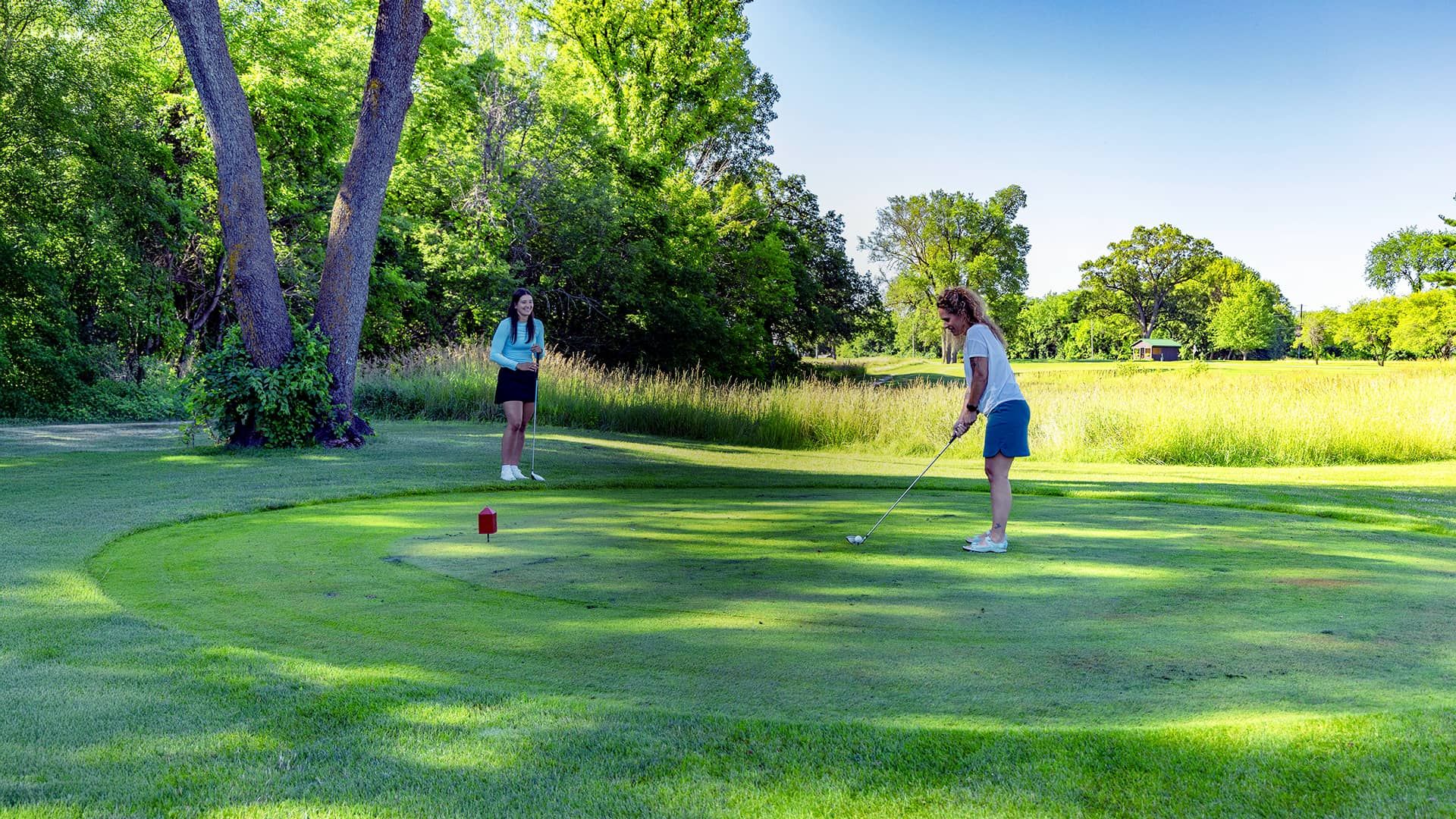 Two girls teeing off at a golf course