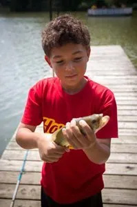 A young boy in a red shirt is holding a fish on a dock.