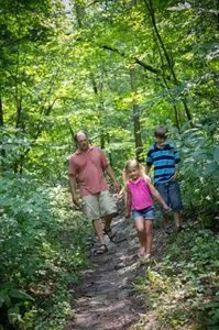 A man and two children are walking down a path in the woods.