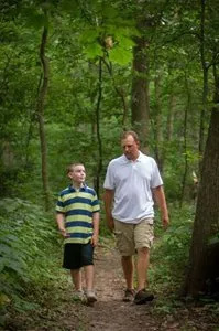 A man and a boy are walking down a path in the woods.