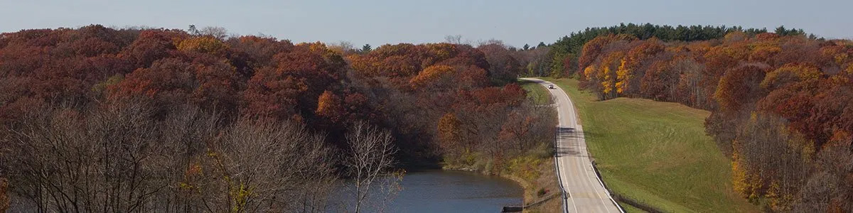 An aerial view of a truck driving down a road next to a river.