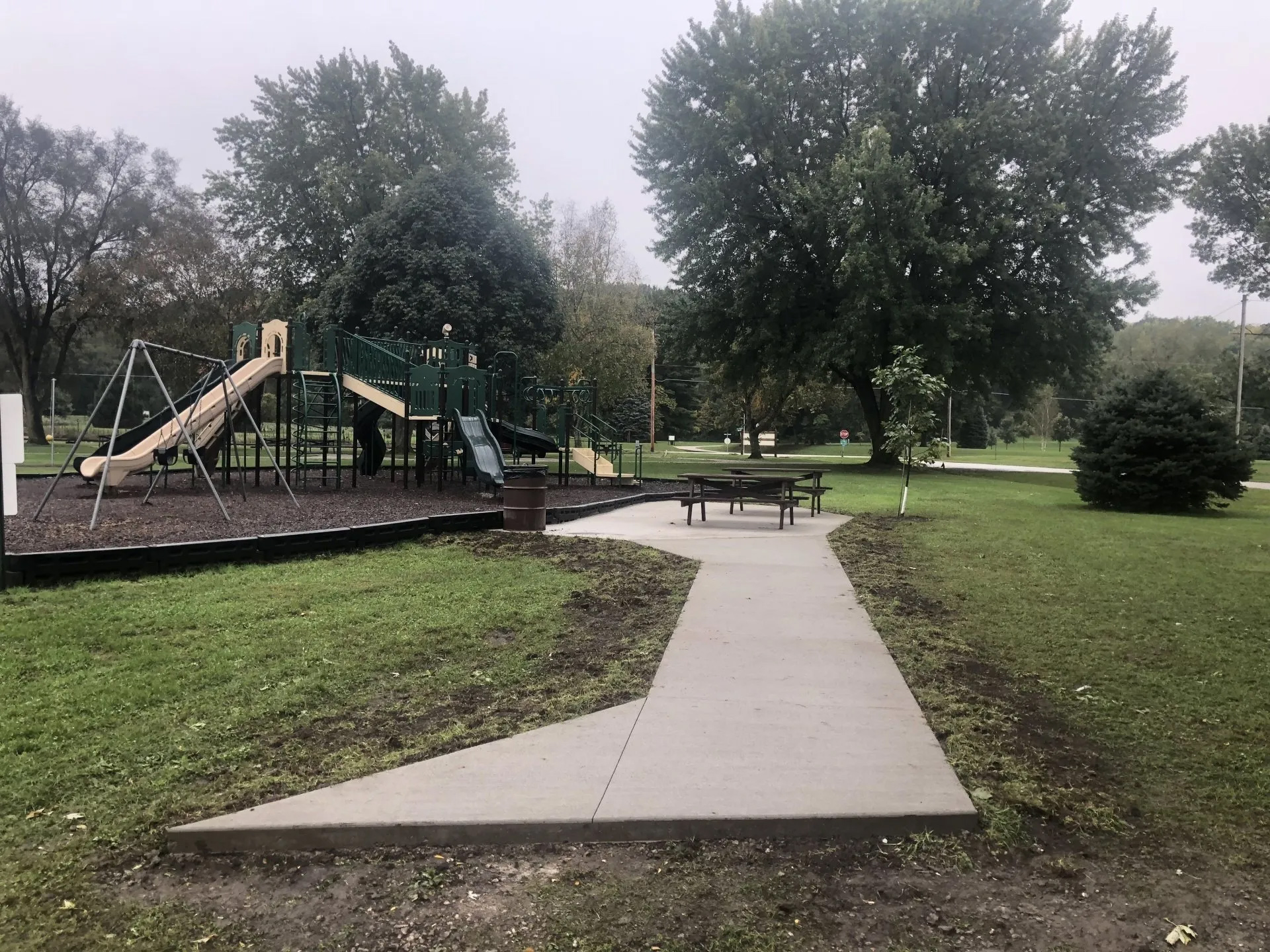 A concrete walkway leading to a playground in a park