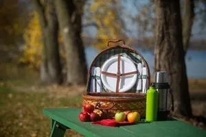 A picnic basket is sitting on a green picnic table.
