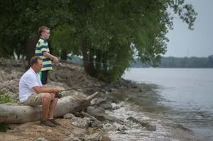A man and a boy are fishing on the shore of a river.