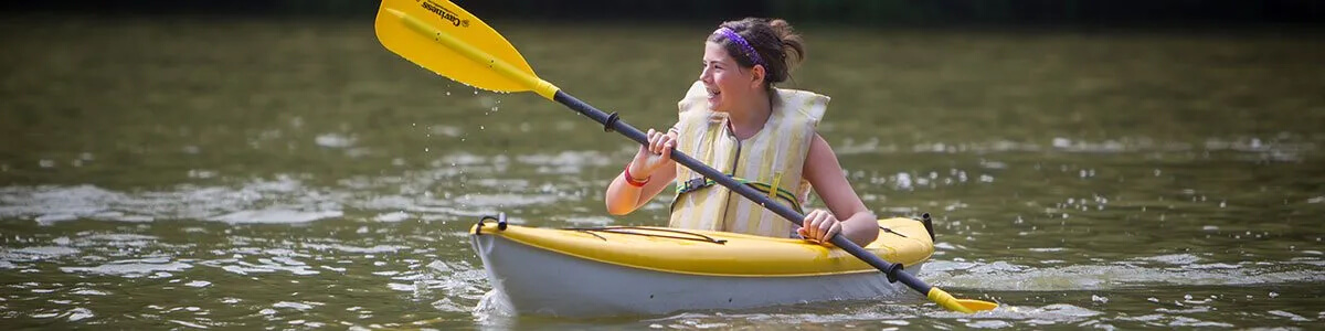 A woman is paddling a yellow kayak on a lake.