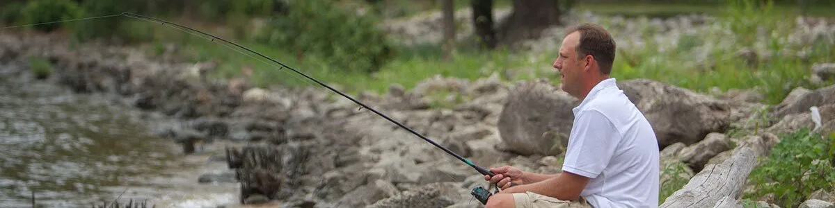 A man is sitting on a rock fishing in a river.
