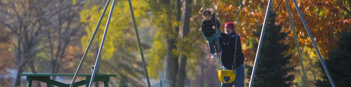 A man and a child are swinging on a swing set in a park.